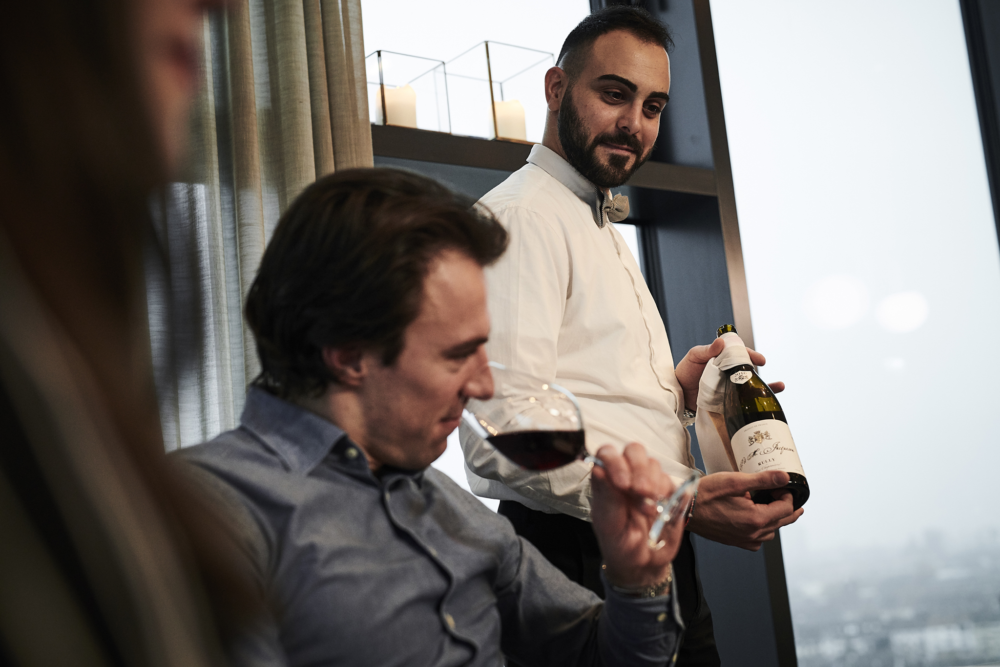 A waiter is presenting a bottle of red wine to a guest, who is tasting it