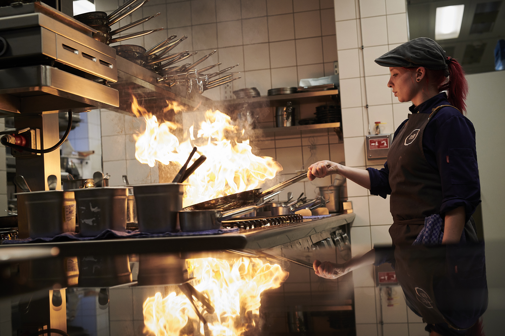 A chef flambés something in a pan on the stove, there is fire in the pan